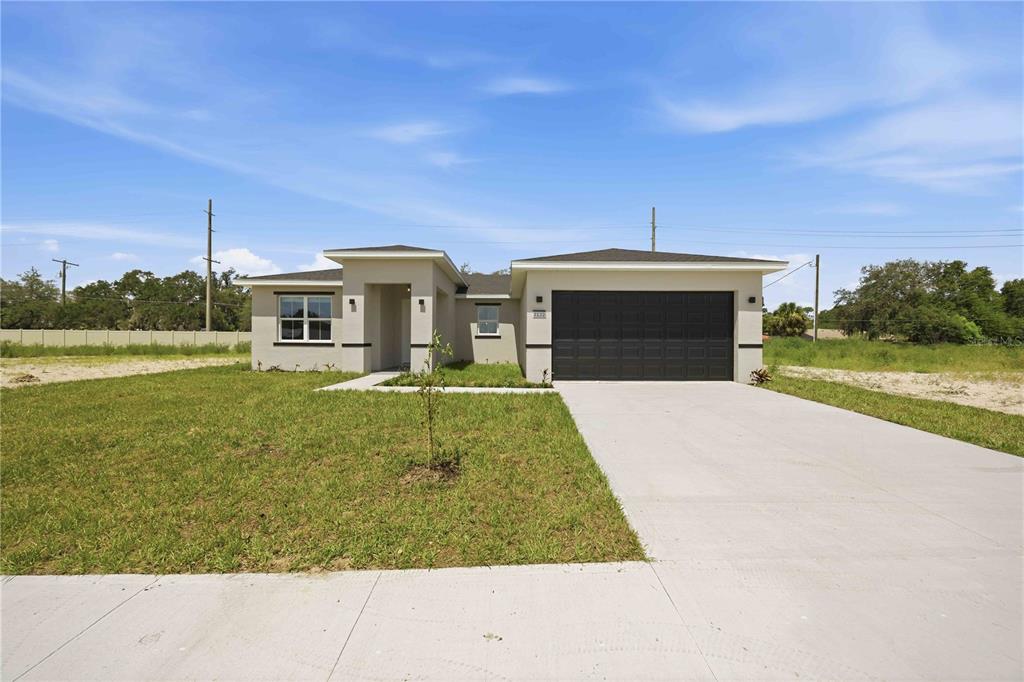 A single-story house with a beige exterior, a dark garage door, and a concrete driveway — 2122 RIVER HAWK LOOP, WINTER HAVEN, FL