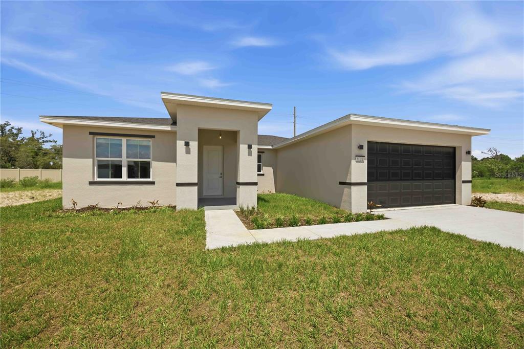 A single-story house with a beige stucco exterior, a dark garage door, and a walkway — 2122 RIVER HAWK LOOP, WINTER HAVEN, FL