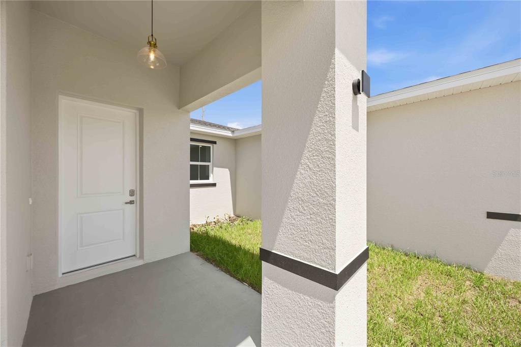 A covered entryway features a white door, a pendant light, and a textured support pillar — 2122 RIVER HAWK LOOP, WINTER HAVEN, FL
