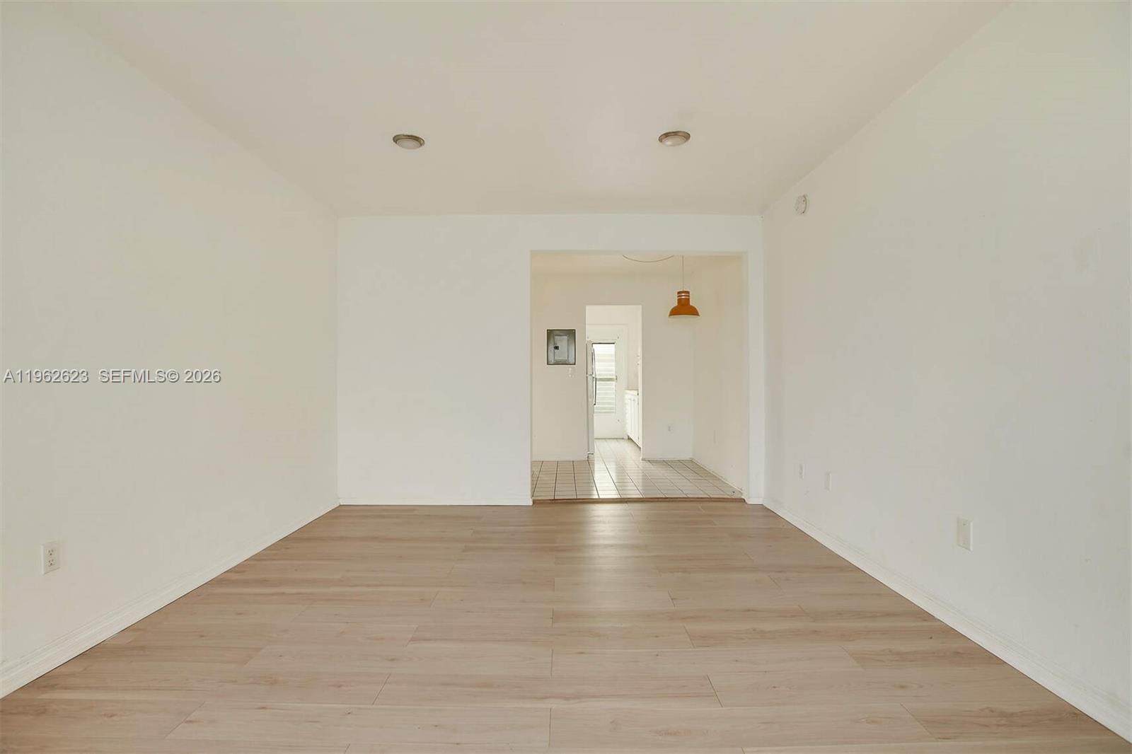 An empty room with light wood-look flooring leads to a tiled kitchen area — 835 Meridian Ave # 3, Miami Beach FL 33139, MIAMI BEACH, FL