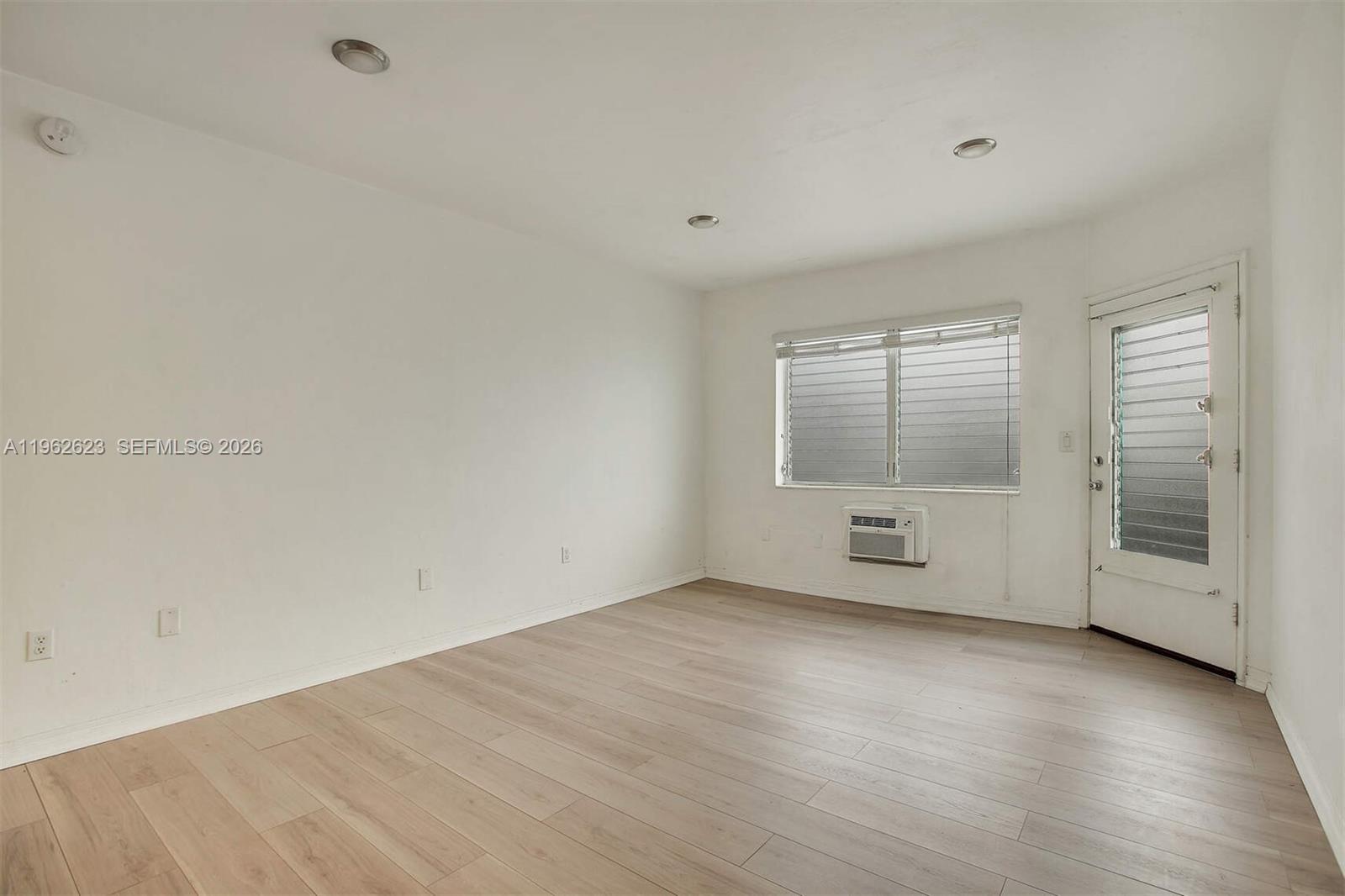 An empty room features white walls, light wood-look flooring, a window, and a door — 835 Meridian Ave # 3, Miami Beach FL 33139, MIAMI BEACH, FL