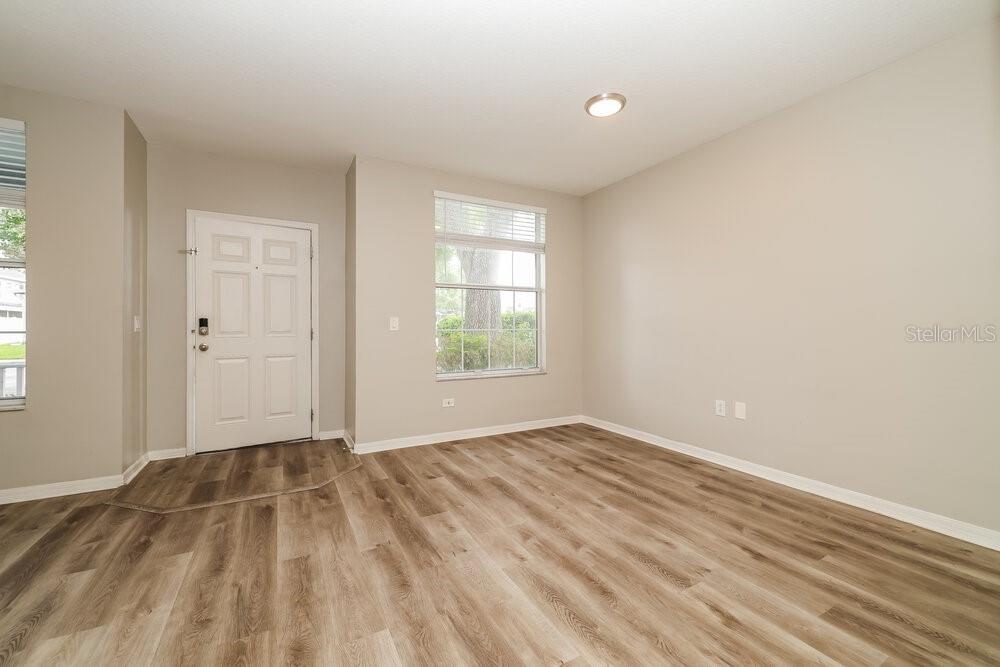 An empty room features light-colored walls, wood-look flooring, a white front door, and windows — 1516 BLUE MAGNOLIA ROAD, BRANDON, FL