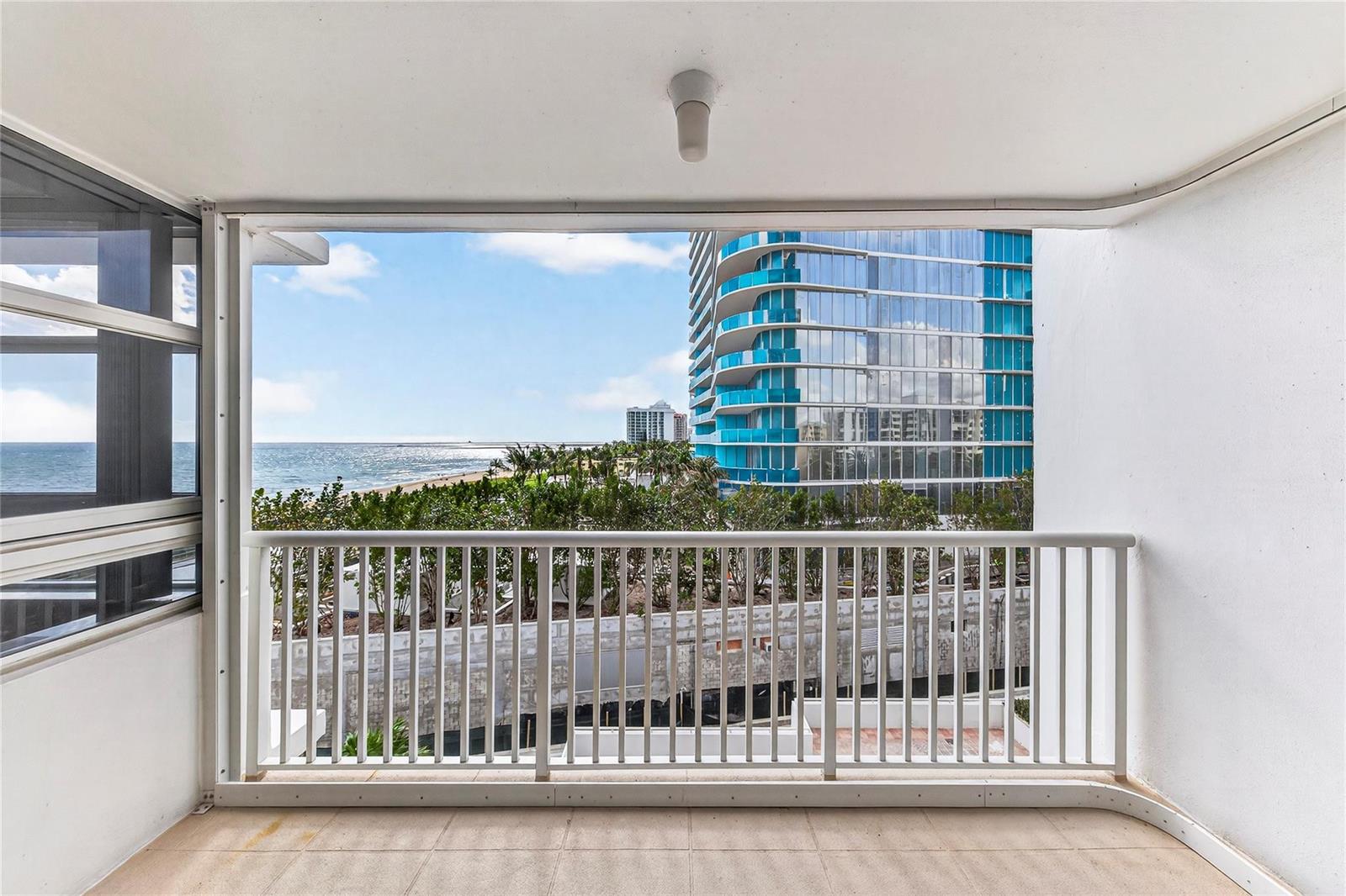 A balcony with a white railing overlooks a beach, palm trees, and a modern glass building — 1370 S Ocean Boulevard # 602, Pompano Beach FL 33062, POMPANO BEACH, FL