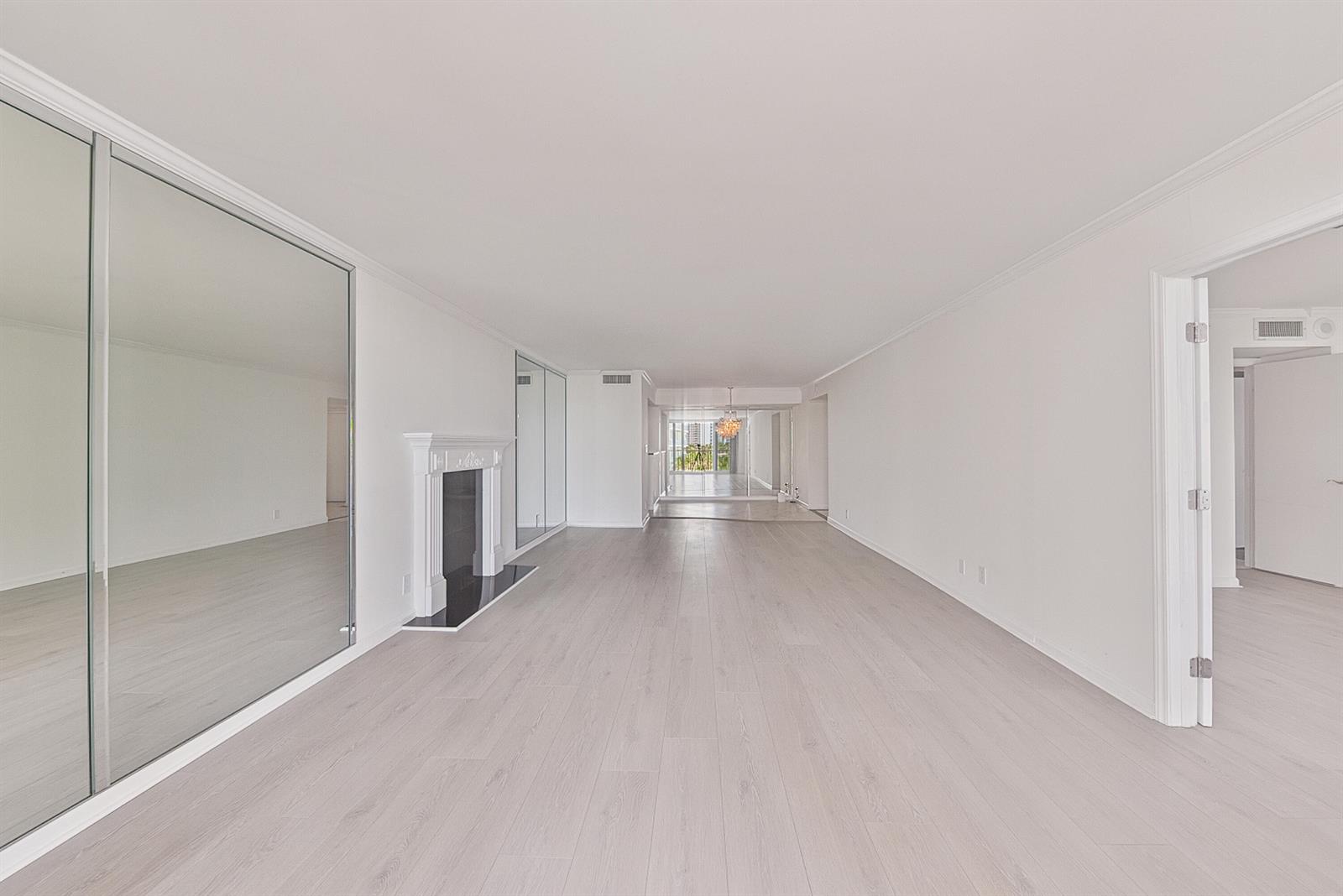 An empty living room features light wood flooring, a white fireplace, and mirrored closet doors — 1370 S Ocean Boulevard # 602, Pompano Beach FL 33062, POMPANO BEACH, FL