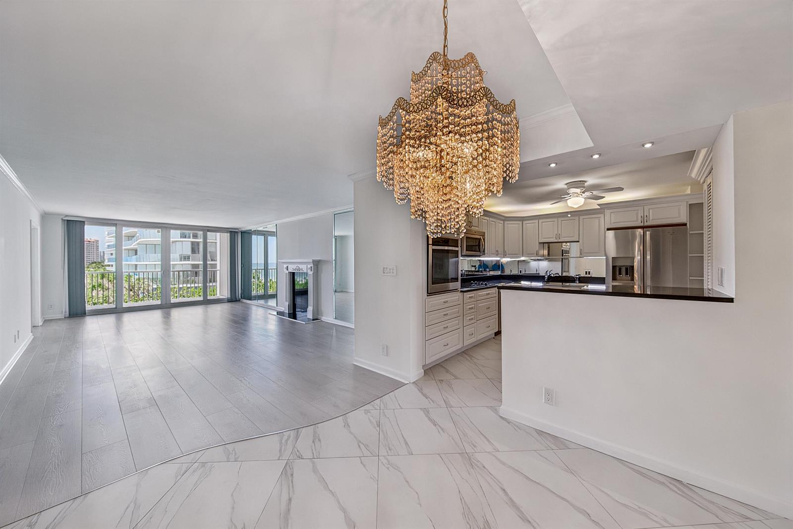 An open-concept living area features a crystal chandelier, marble-look tile flooring, and a modern kitchen — 1370 S Ocean Boulevard # 602, Pompano Beach FL 33062, POMPANO BEACH, FL