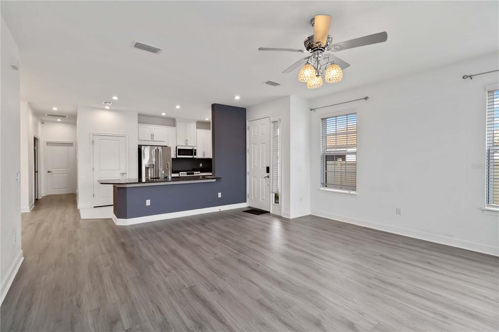 An open-concept living area features light wood-look flooring, a kitchen with dark blue accents, and a ceiling fan — 10934 WENDOVER DRIVE, PALMETTO, FL