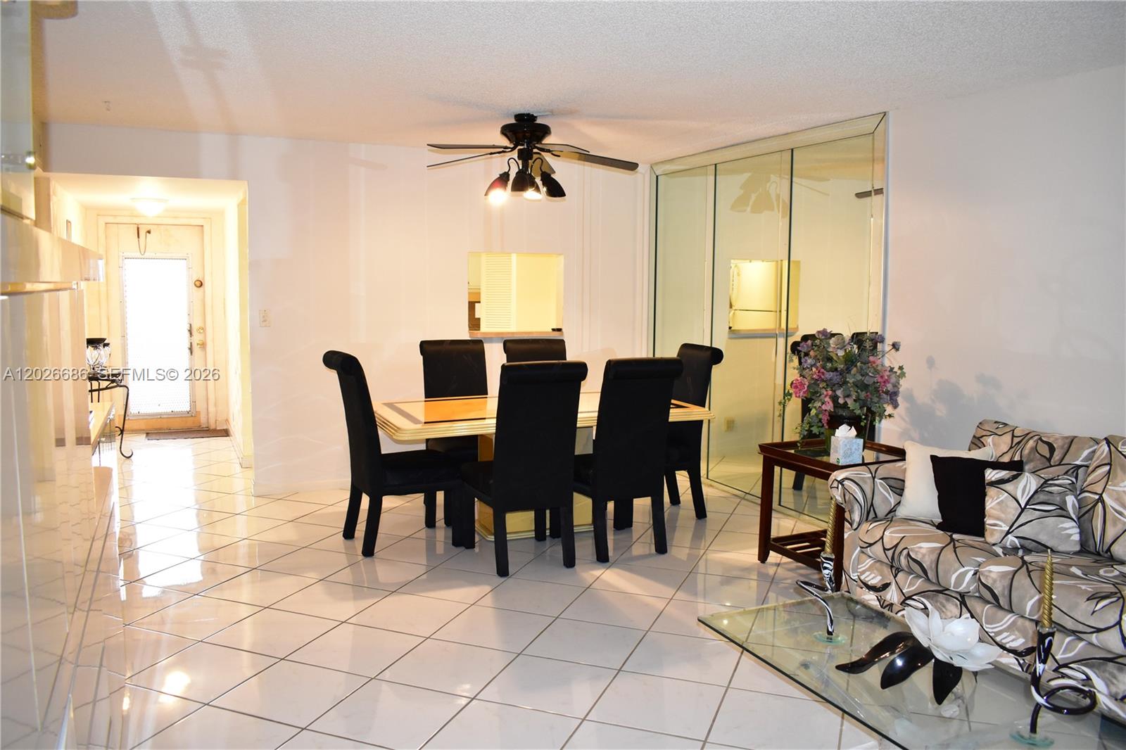 A dining area with black chairs and a glass table sits beside a living room — 9461 Sunrise Lakes Blvd # 103, Sunrise FL 33322, SUNRISE, FL
