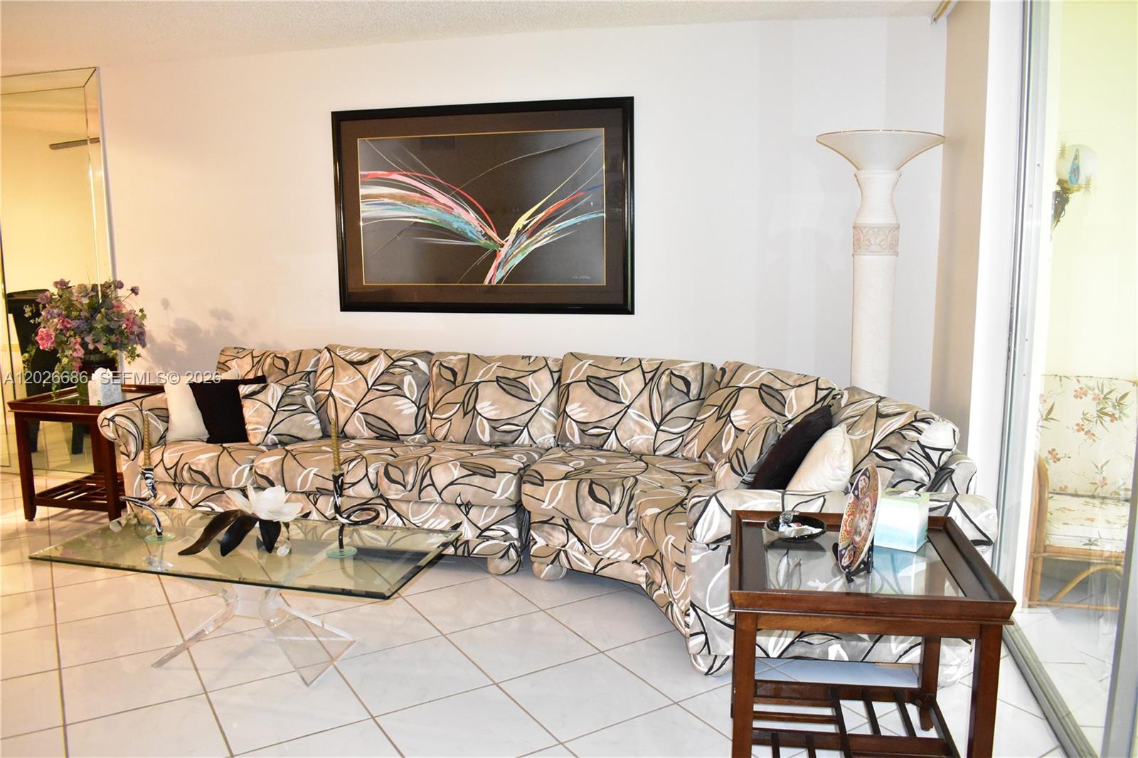 A living room features a patterned sectional sofa, a glass coffee table, and tile flooring — 9461 Sunrise Lakes Blvd # 103, Sunrise FL 33322, SUNRISE, FL