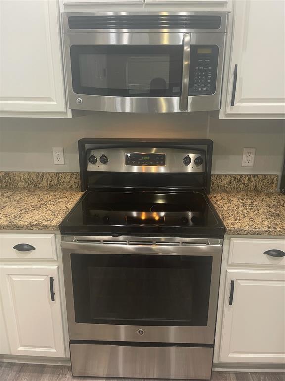 A stainless steel microwave and electric range are installed between white kitchen cabinets — 30823 SATINLEAF RUN, BROOKSVILLE, FL