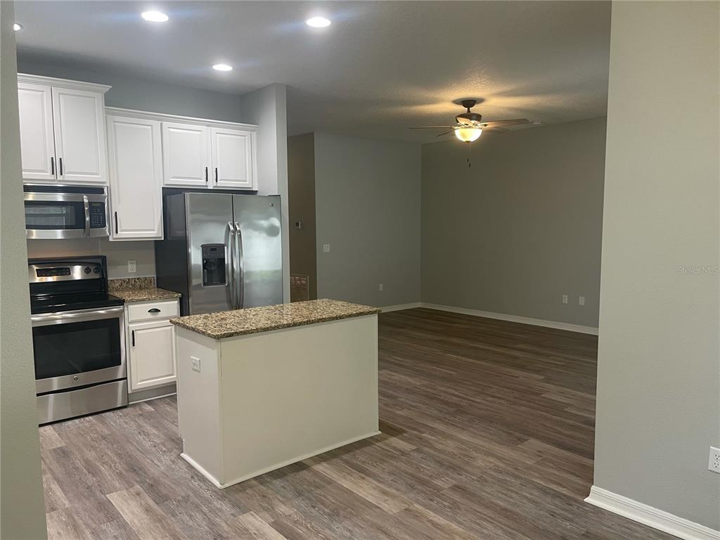 A kitchen with white cabinets, stainless steel appliances, and a granite island opens to a living area — 30823 SATINLEAF RUN, BROOKSVILLE, FL