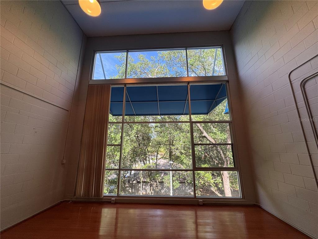 A room with high ceilings, block walls, hardwood floors, and a large window with an awning — 2515 SW 35TH PLACE UNIT 209, GAINESVILLE, FL
