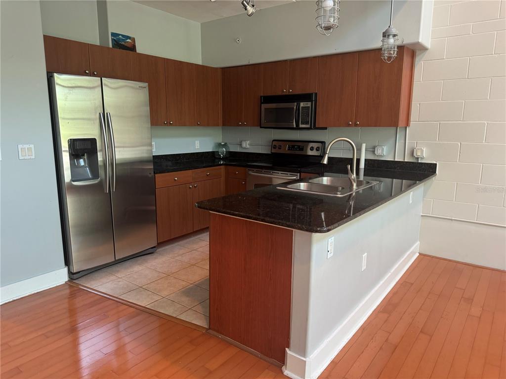 A kitchen features wood cabinets, dark granite countertops, stainless steel appliances, and hardwood flooring — 2515 SW 35TH PLACE UNIT 209, GAINESVILLE, FL