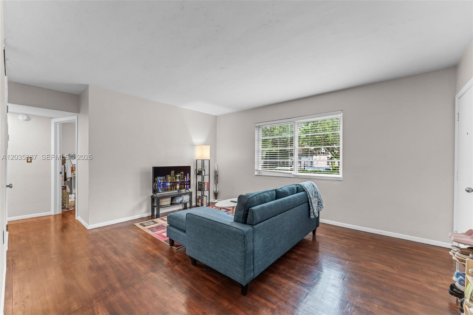 A living room features a blue sofa, hardwood floors, and a window with blinds — 5685 SW 80th St # 58B, Miami FL 33143, MIAMI, FL