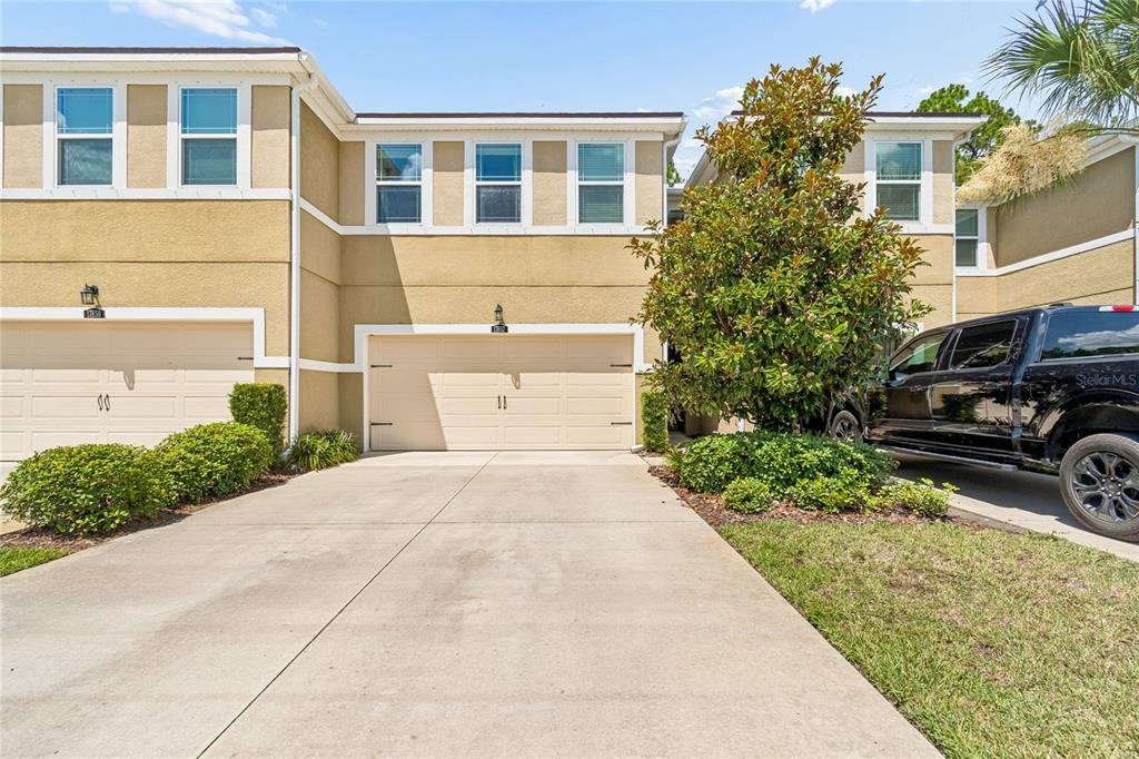 A two-story townhouse exterior features a beige stucco facade, a two-car garage, and a driveway — 17852 ALTHEA BLUE PLACE, LUTZ, FL