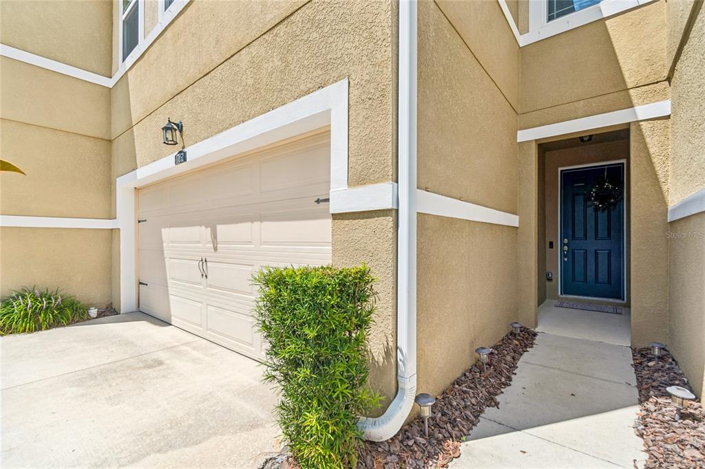 A beige stucco townhouse exterior features a two-car garage and a dark blue front door — 17852 ALTHEA BLUE PLACE, LUTZ, FL