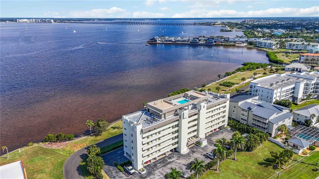 An aerial view shows a multi-story apartment building with a rooftop pool near the water — 1500 PARK BEACH CIRCLE UNIT 6C, PUNTA GORDA, FL