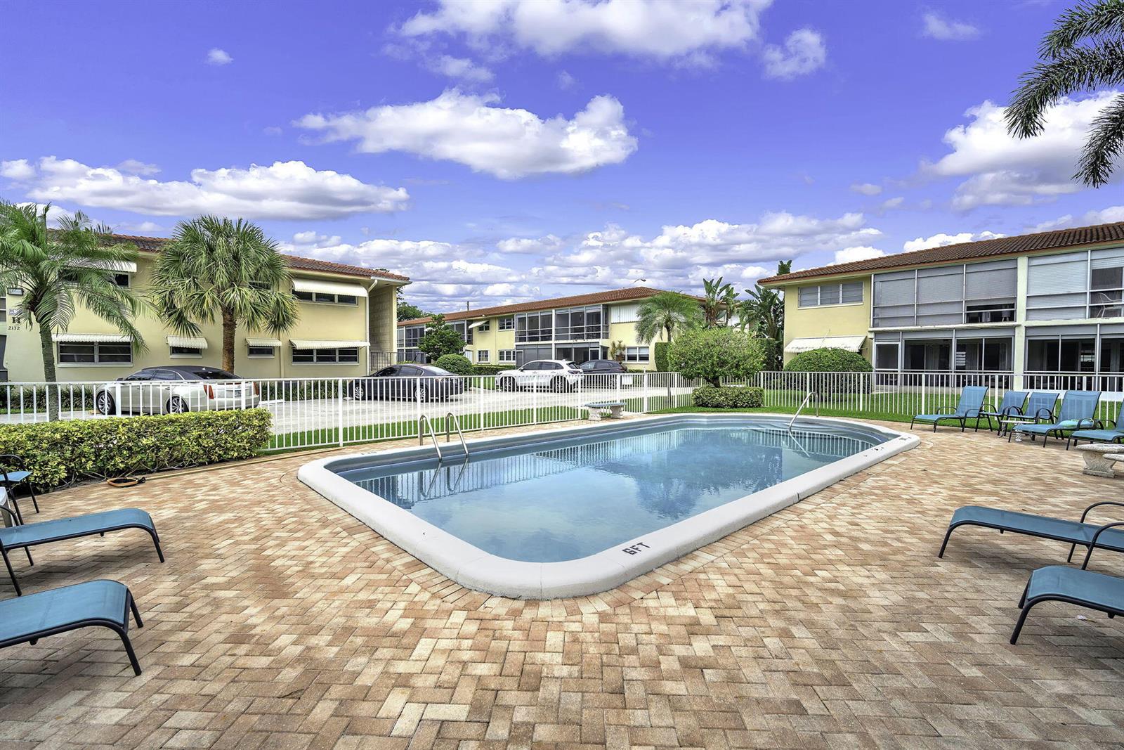 A rectangular swimming pool sits on a brick patio surrounded by apartment buildings and landscaping — 2130 NE 36th Street # 63, Lighthouse Point FL 33064, LIGHTHOUSE POINT, FL