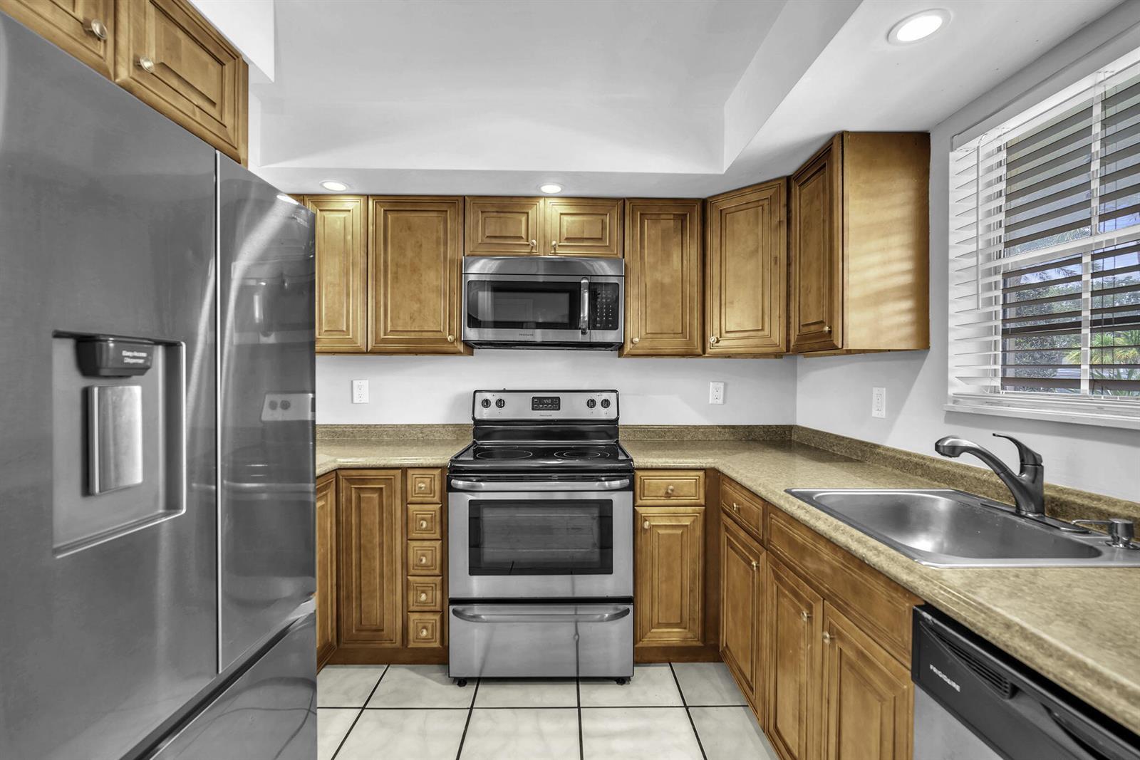 A kitchen features wood cabinets, stainless steel appliances, a beige countertop, and white tile flooring — 2130 NE 36th Street # 63, Lighthouse Point FL 33064, LIGHTHOUSE POINT, FL