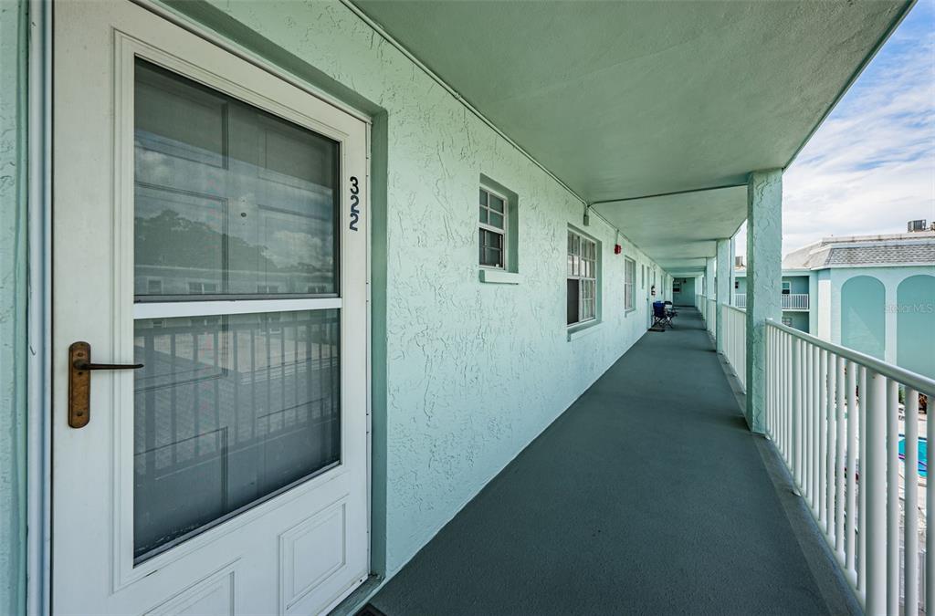An exterior view of a teal apartment building hallway with a screen door numbered 322 — 1706 BELLEAIR FOREST DRIVE UNIT 322, BELLEAIR, FL
