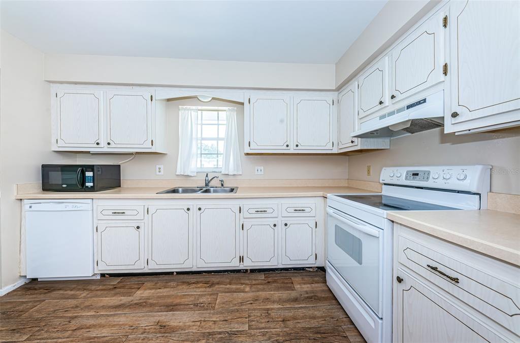 A kitchen features white cabinets, laminate countertops, a white stove, and wood-look flooring — 1706 BELLEAIR FOREST DRIVE UNIT 322, BELLEAIR, FL