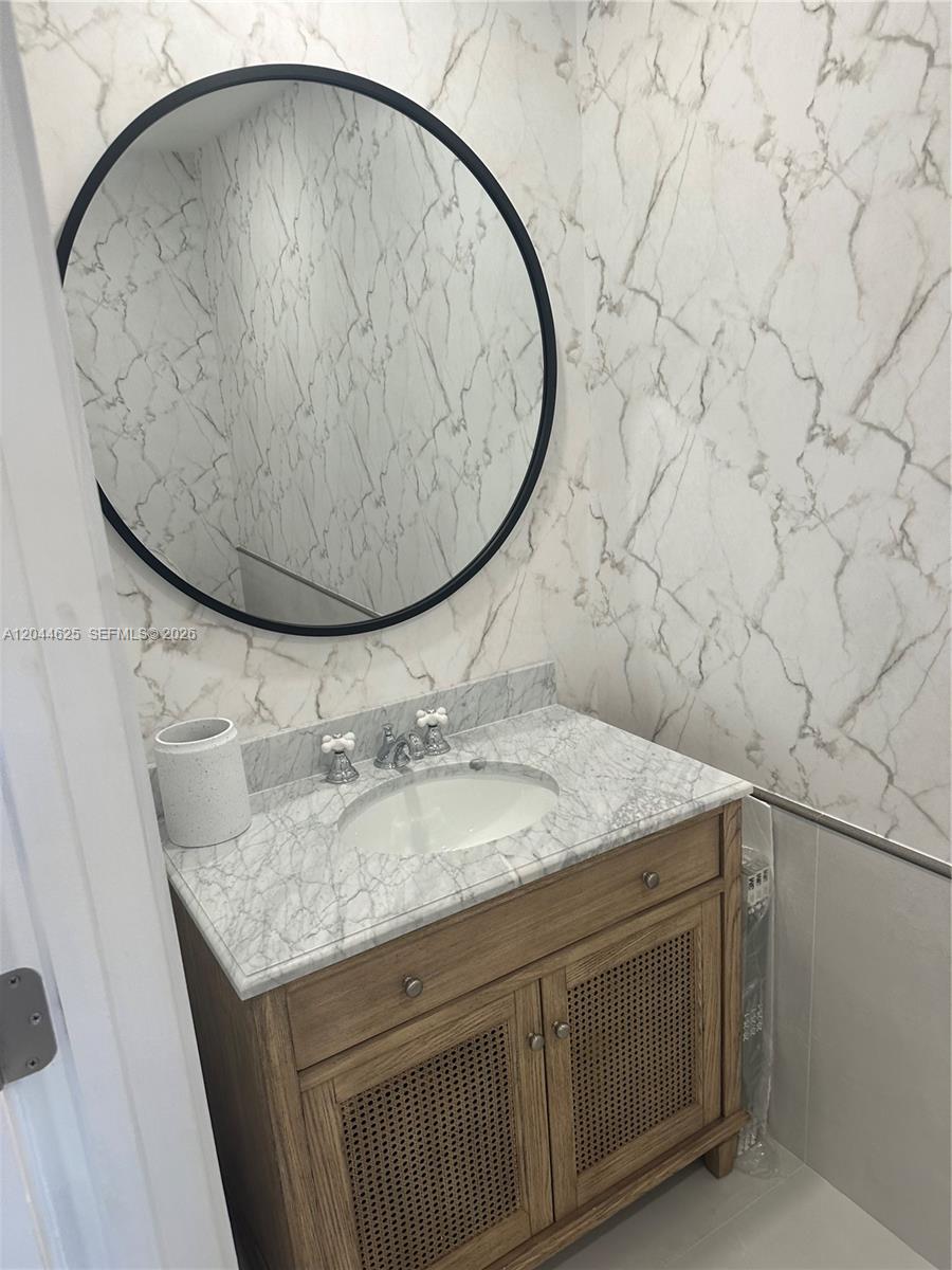 A bathroom features a wooden vanity with a marble countertop, a round mirror, and marble-patterned wallpaper — 1060 Brickell Ave # 2505, Miami FL 33131, MIAMI, FL