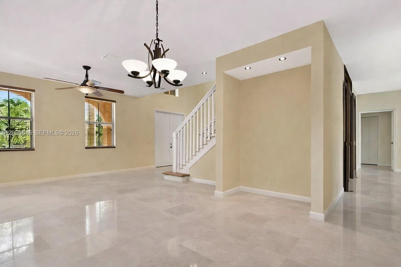 An empty room features light-colored tile flooring, a staircase, a chandelier, and a ceiling fan — 1319 Croton Ct, Weston FL 33327, WESTON, FL