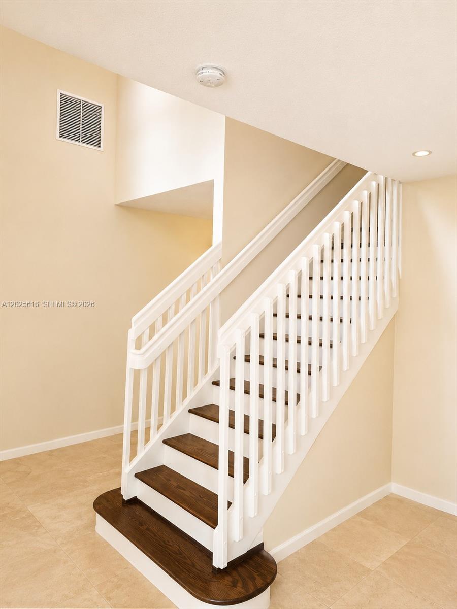 A staircase with dark wood treads and white railings ascends against a beige wall — 1319 Croton Ct, Weston FL 33327, WESTON, FL