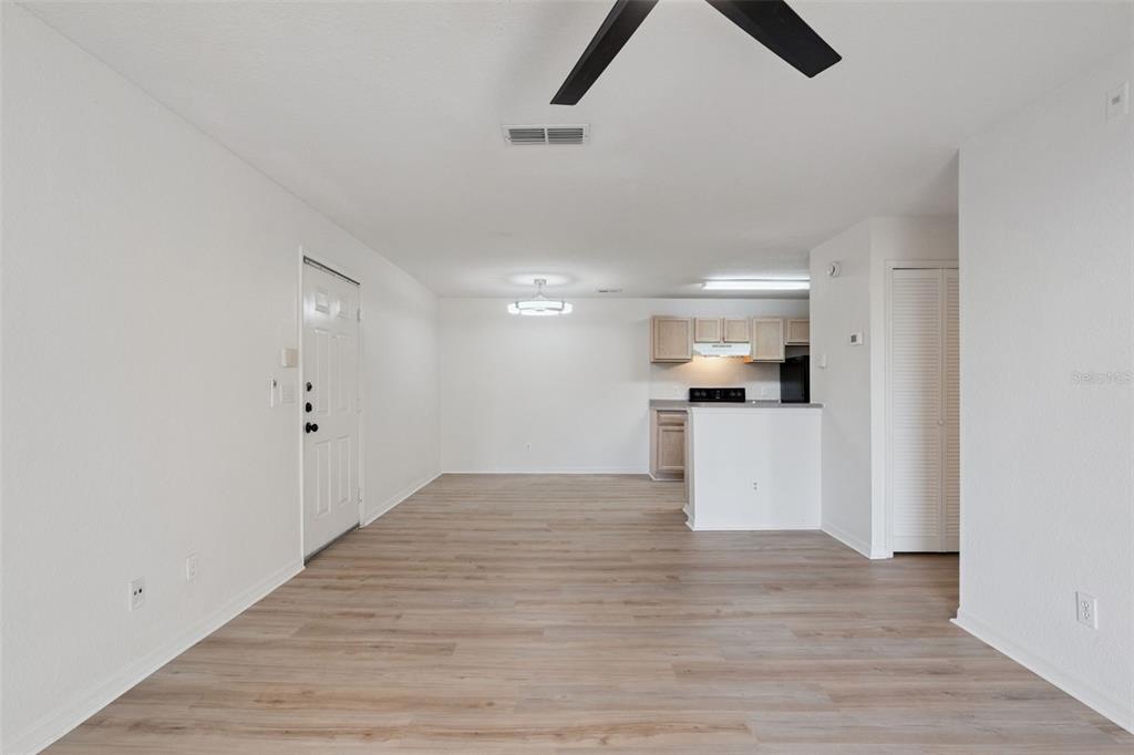 An open-concept living area features light wood-look flooring, white walls, and an adjacent kitchen — 8813 LATREC AVENUE UNIT 206, ORLANDO, FL