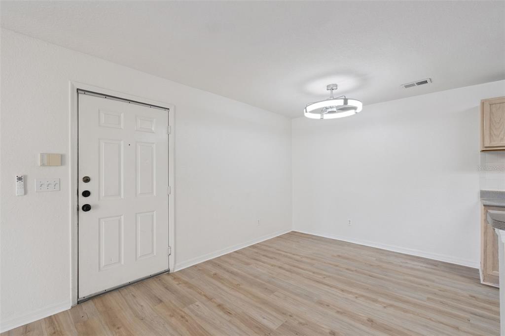 A bright, empty room features white walls, light wood-look flooring, and a modern ceiling light — 8813 LATREC AVENUE UNIT 206, ORLANDO, FL
