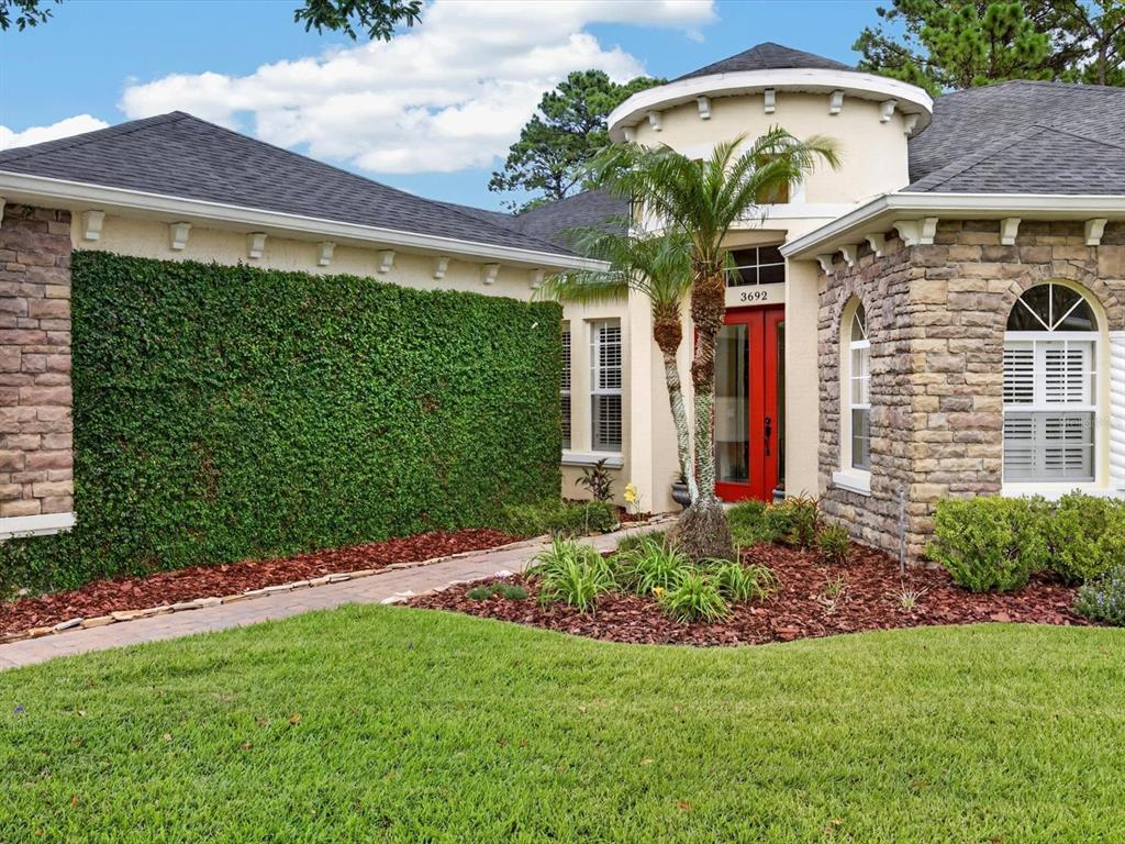 A single-story house exterior features a red front door, stone accents, and a green ivy wall — 3692 HEIRLOOM ROSE PLACE, OVIEDO, FL