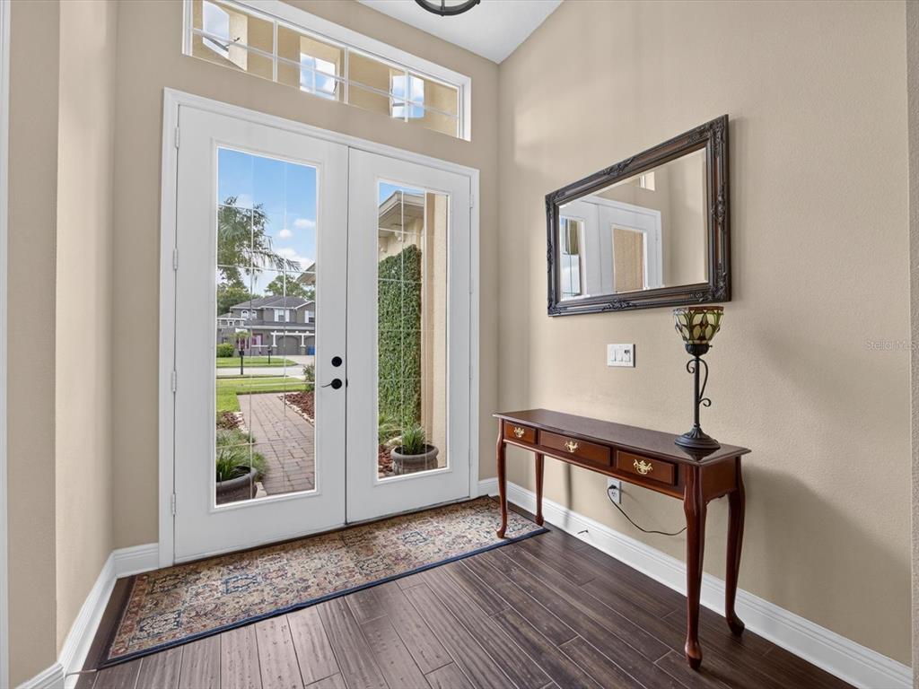 An entryway features a double glass door, dark wood flooring, a console table, and a mirror — 3692 HEIRLOOM ROSE PLACE, OVIEDO, FL