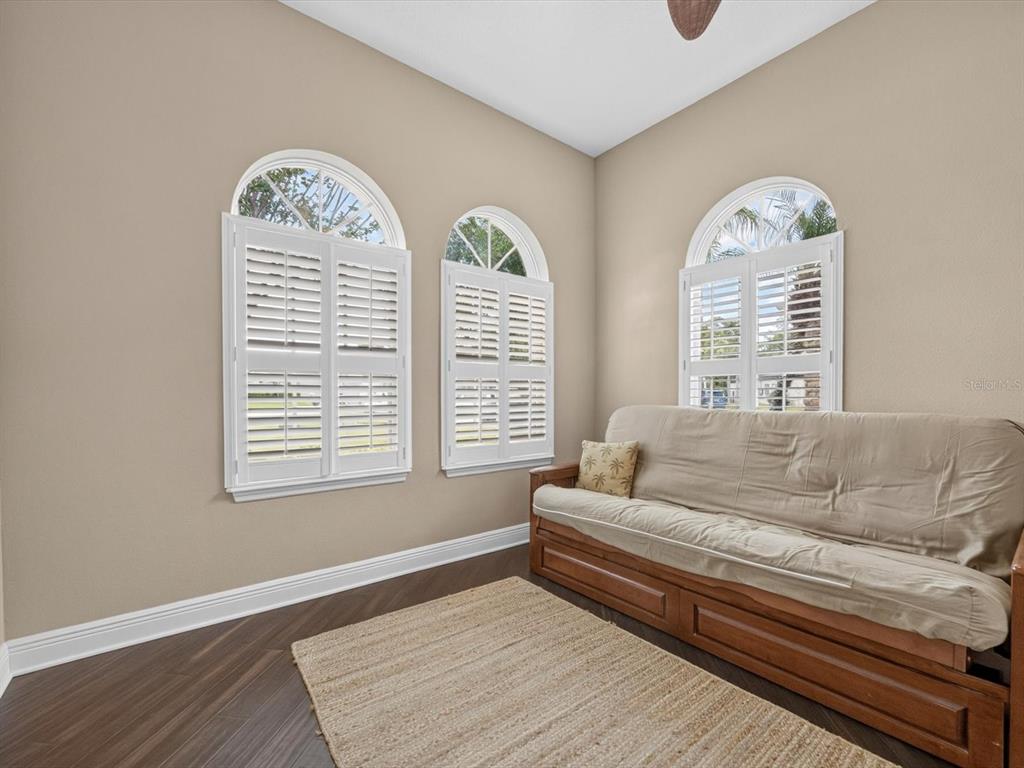 A room with beige walls, dark wood floors, three arched windows, and a wooden futon — 3692 HEIRLOOM ROSE PLACE, OVIEDO, FL