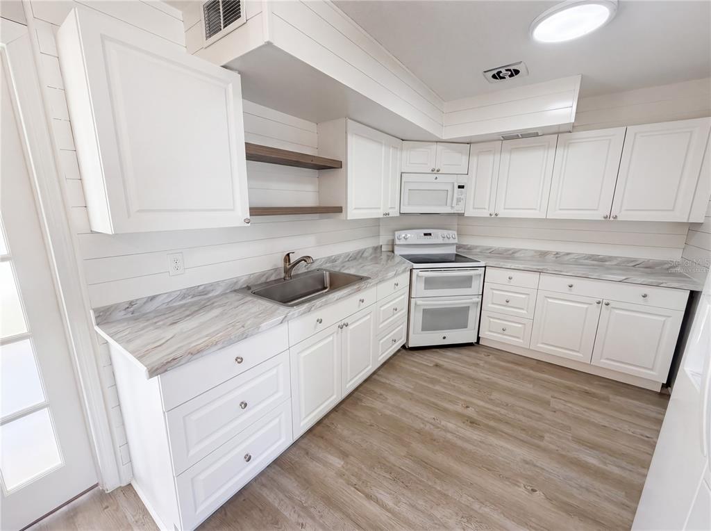A kitchen features white cabinets, wood-look flooring, marble-patterned countertops, and open shelving — 7328 TANGELO AVENUE, PORT RICHEY, FL