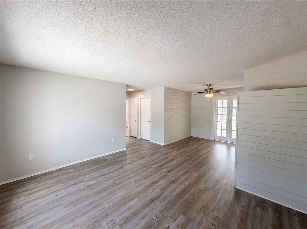 An interior view of a living area with wood-look flooring, shiplap walls, and French doors — 7328 TANGELO AVENUE, PORT RICHEY, FL