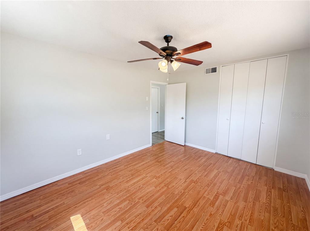 An empty bedroom with light gray walls, wood-look flooring, a ceiling fan, and white closets — 7328 TANGELO AVENUE, PORT RICHEY, FL