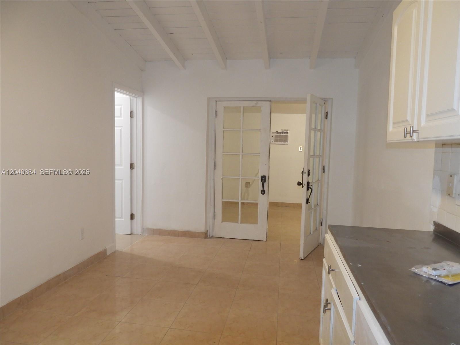 A kitchen area with tile flooring, white cabinets, and French doors leading to another room — MIAMI, FL