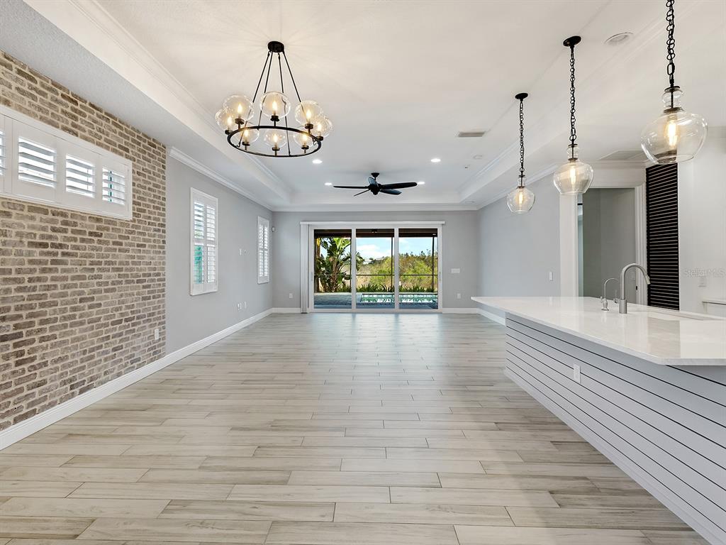 A bright, open-concept living area features a brick accent wall, wood-look flooring, and kitchen island — 1010 CROSSWIND AVENUE, SARASOTA, FL