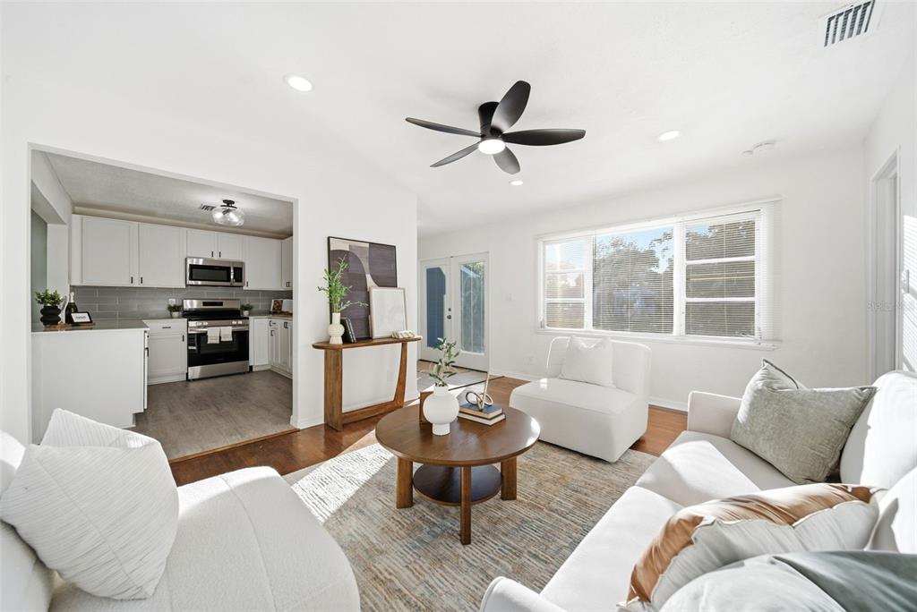 A bright living room features white furniture, a round wooden coffee table, and an adjacent kitchen — 3007 KNOLLWOOD CIRCLE, ORLANDO, FL