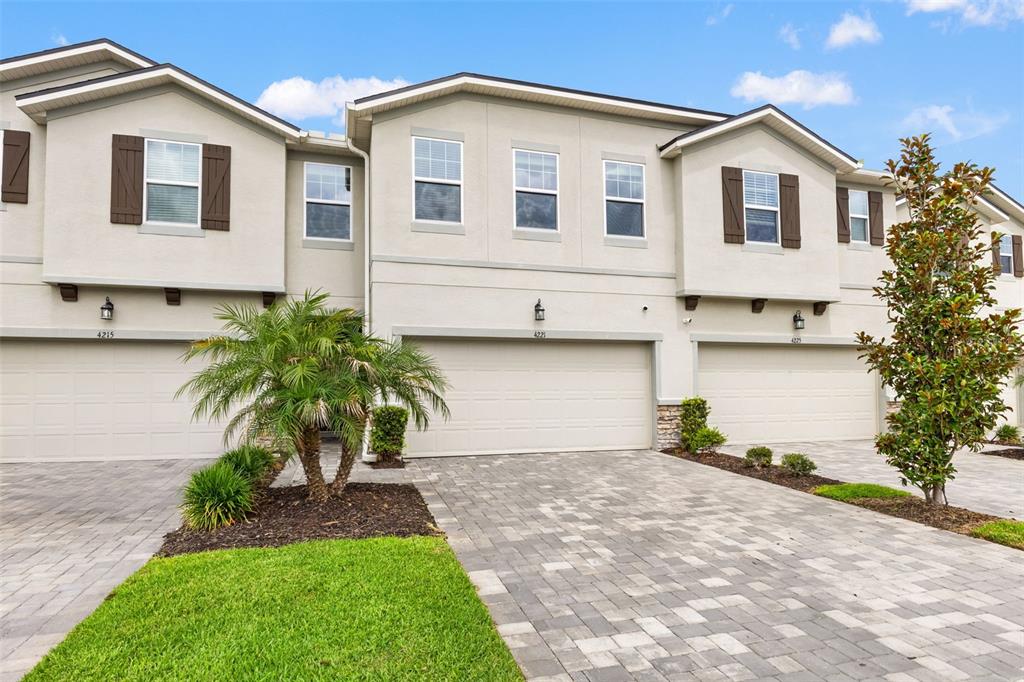 A row of three-story townhomes features beige stucco exteriors, brown shutters, and paved driveways — 4221 CLOUD HOPPER WAY, LUTZ, FL