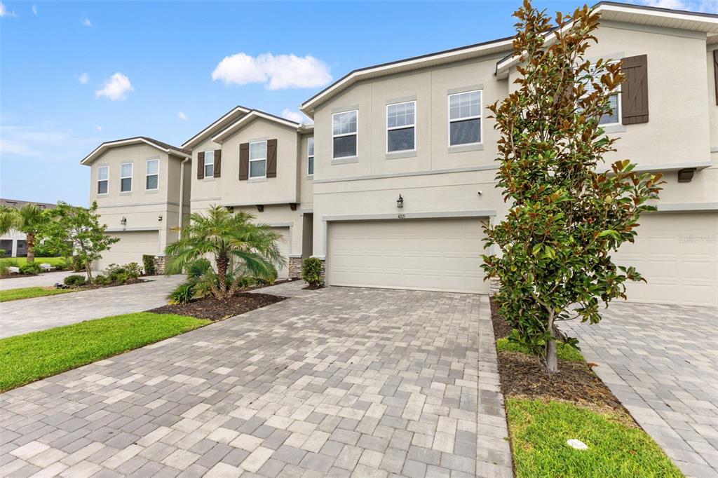 A view of the exterior of a multi-unit townhouse complex with paved driveways and garages — 4221 CLOUD HOPPER WAY, LUTZ, FL