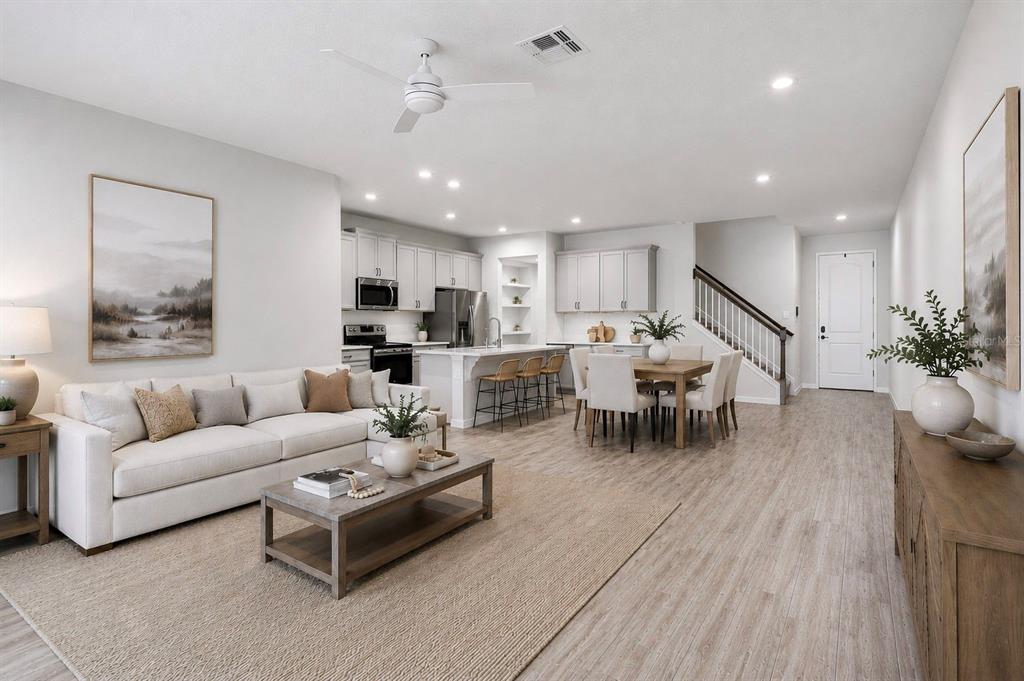 An open-concept living room and kitchen featuring light wood floors, white cabinetry, and neutral decor — 4221 CLOUD HOPPER WAY, LUTZ, FL