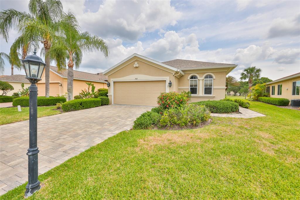 A single-story house with a beige stucco exterior, a two-car garage, and a paved driveway — 1907 STERLING GLEN COURT, SUN CITY CENTER, FL