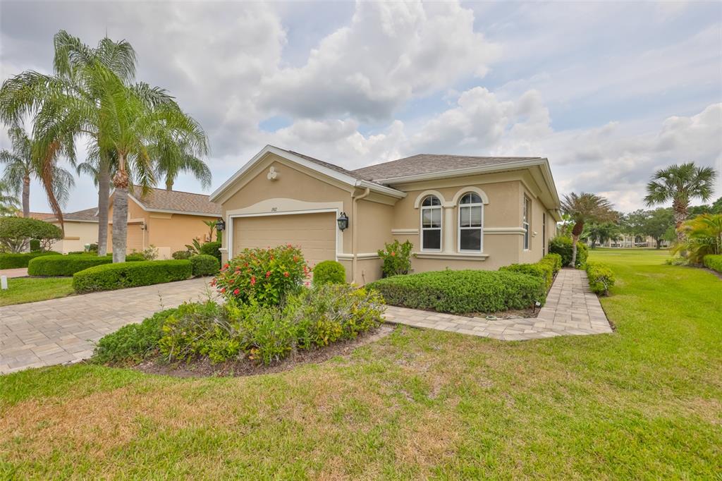 A tan, single-story house with a two-car garage, arched windows, and a paved walkway — 1907 STERLING GLEN COURT, SUN CITY CENTER, FL