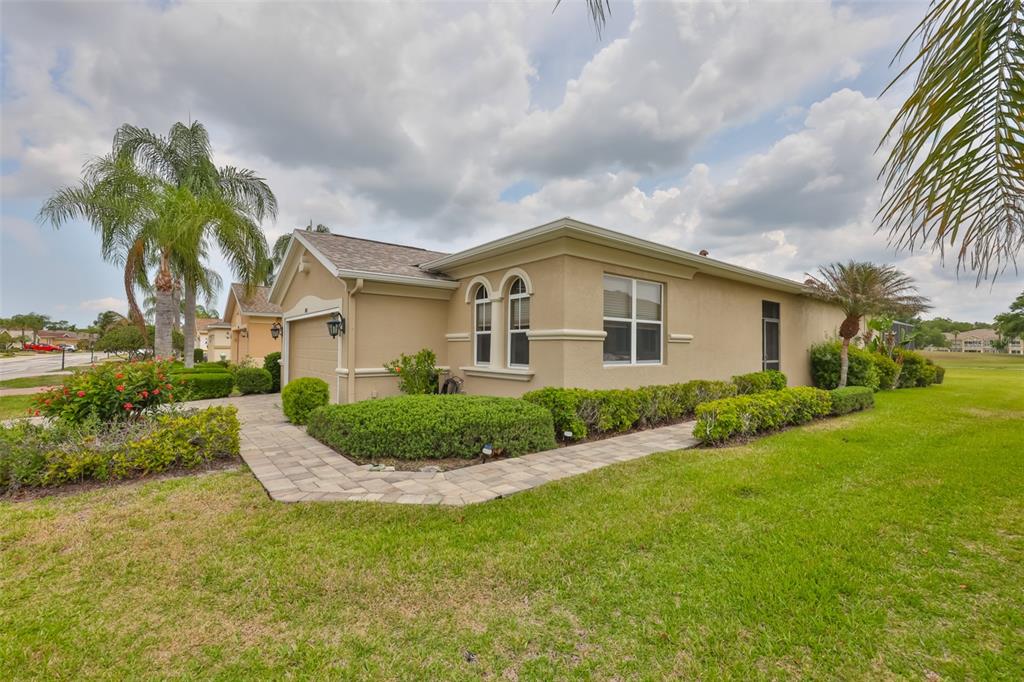 A tan, single-story house with a paved walkway, manicured hedges, and palm trees — 1907 STERLING GLEN COURT, SUN CITY CENTER, FL