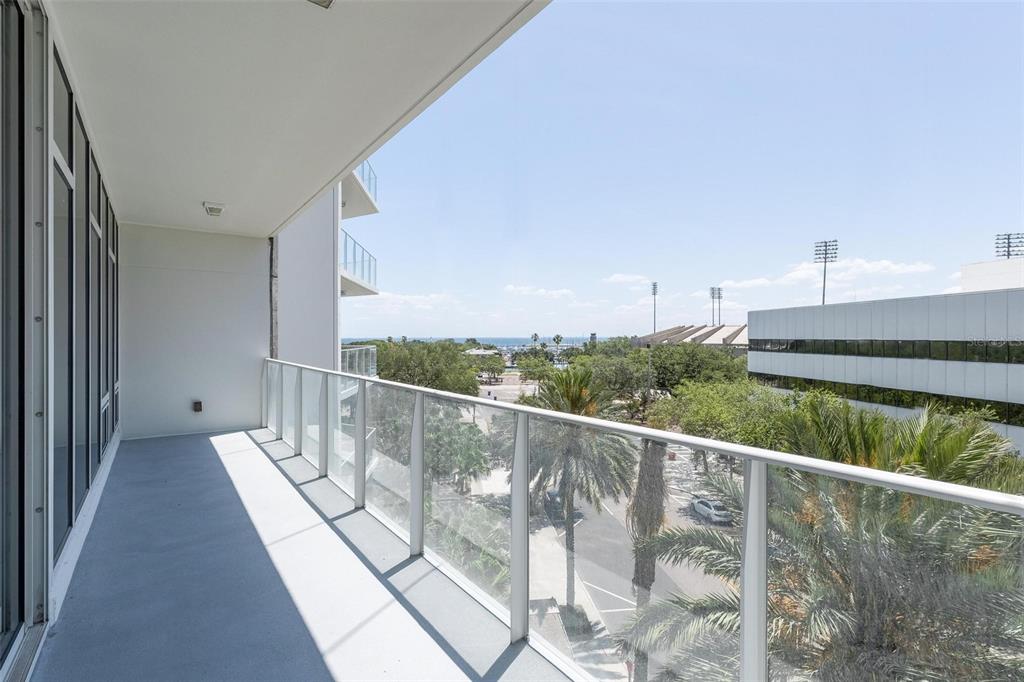 A balcony with a glass railing overlooks a parking lot, palm trees, and the distant ocean — 175 1ST STREET S UNIT 504, ST PETERSBURG, FL