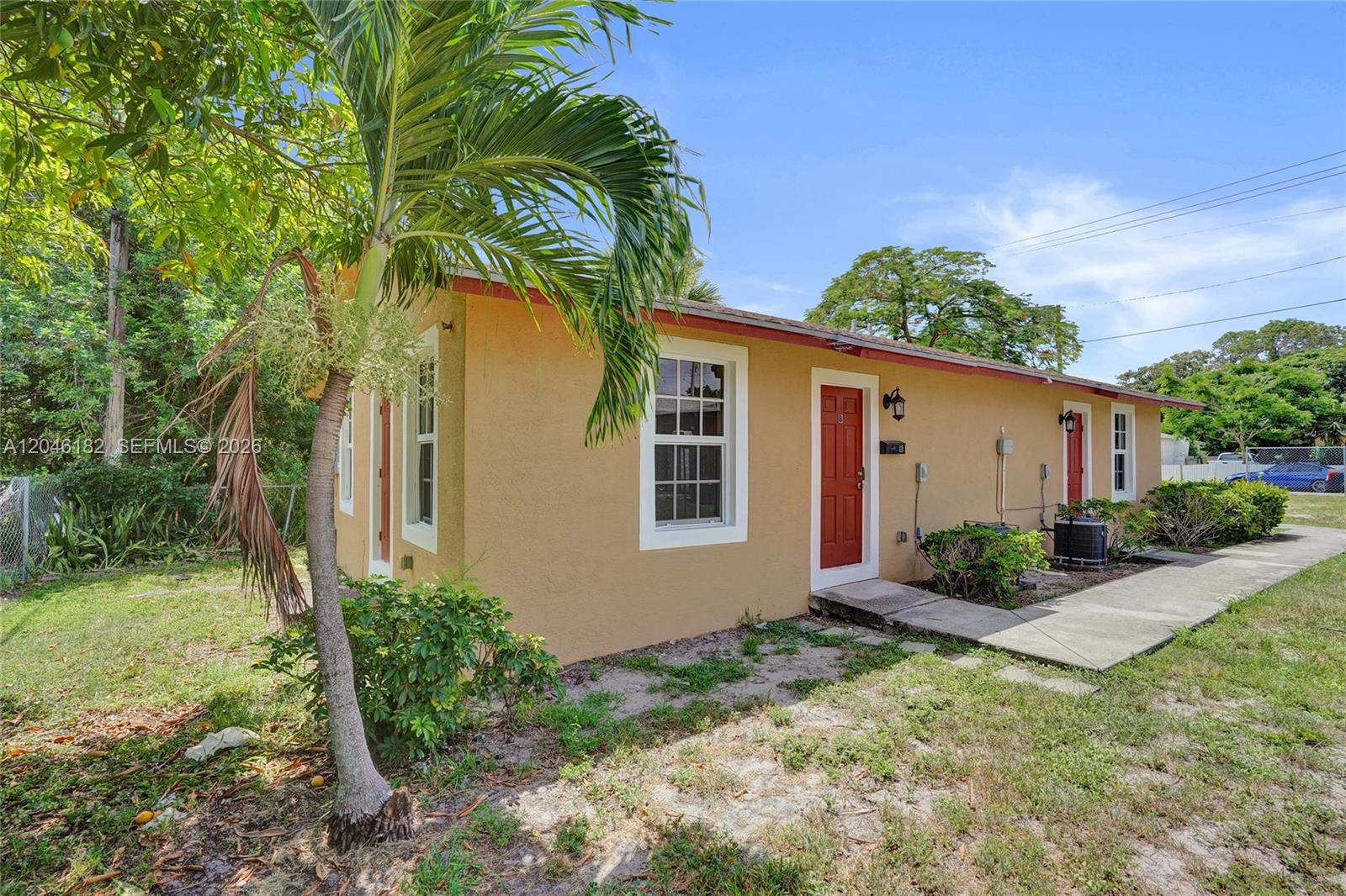 A single-story tan stucco building features two red front doors and a palm tree — 727 22nd St # B, West Palm Beach FL 33407, WEST PALM BEACH, FL