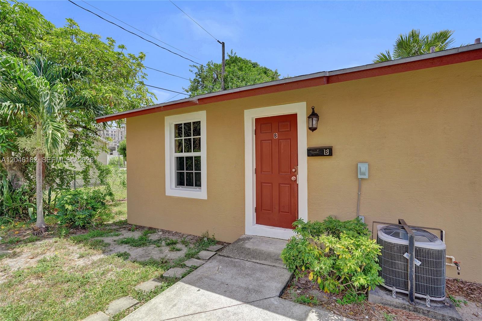 A tan exterior wall features a red door labeled B, a window, and an air conditioner — 727 22nd St # B, West Palm Beach FL 33407, WEST PALM BEACH, FL