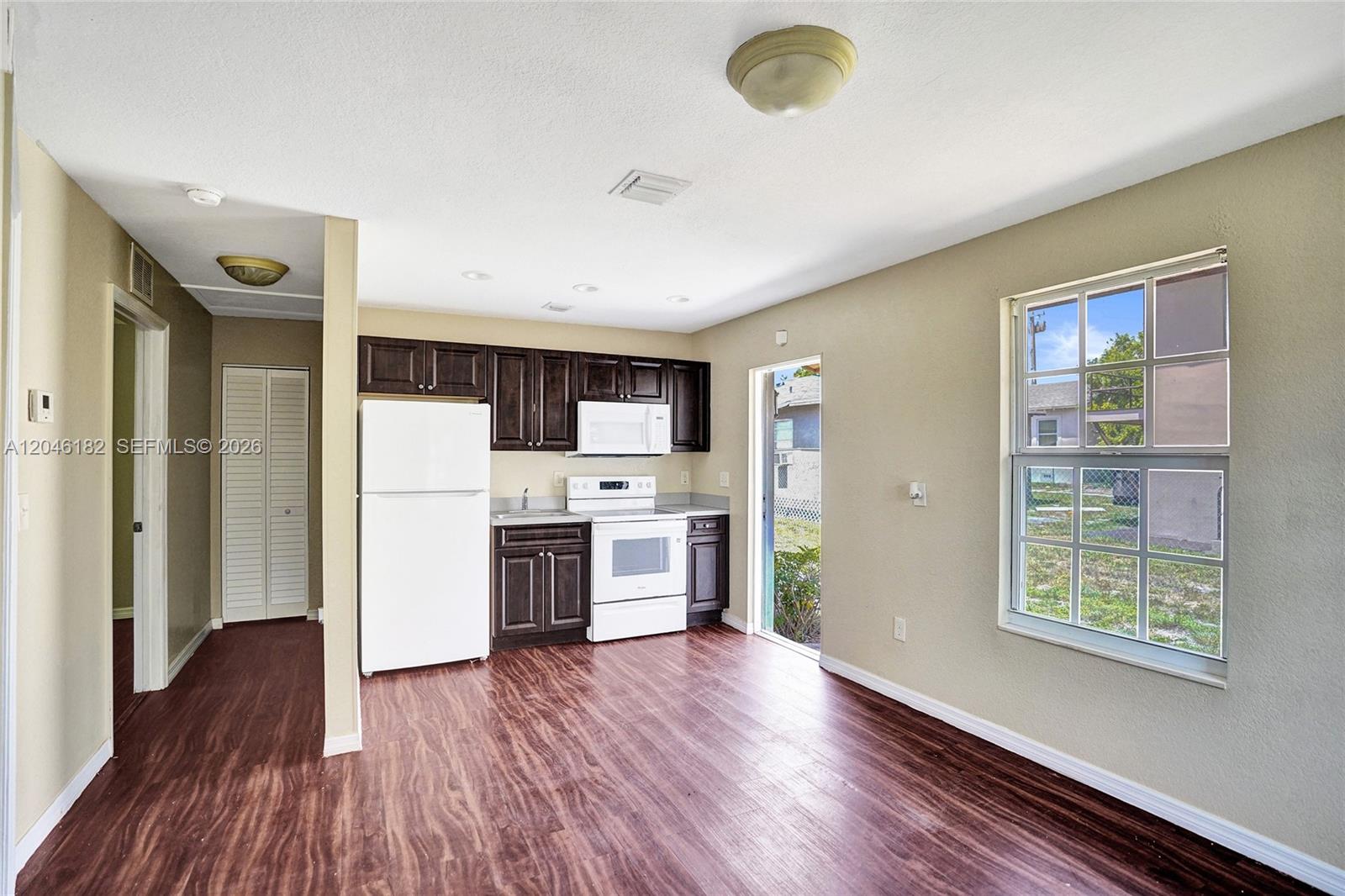 A kitchen features dark wood cabinets, white appliances, and wood-look flooring in an open space — 727 22nd St # B, West Palm Beach FL 33407, WEST PALM BEACH, FL