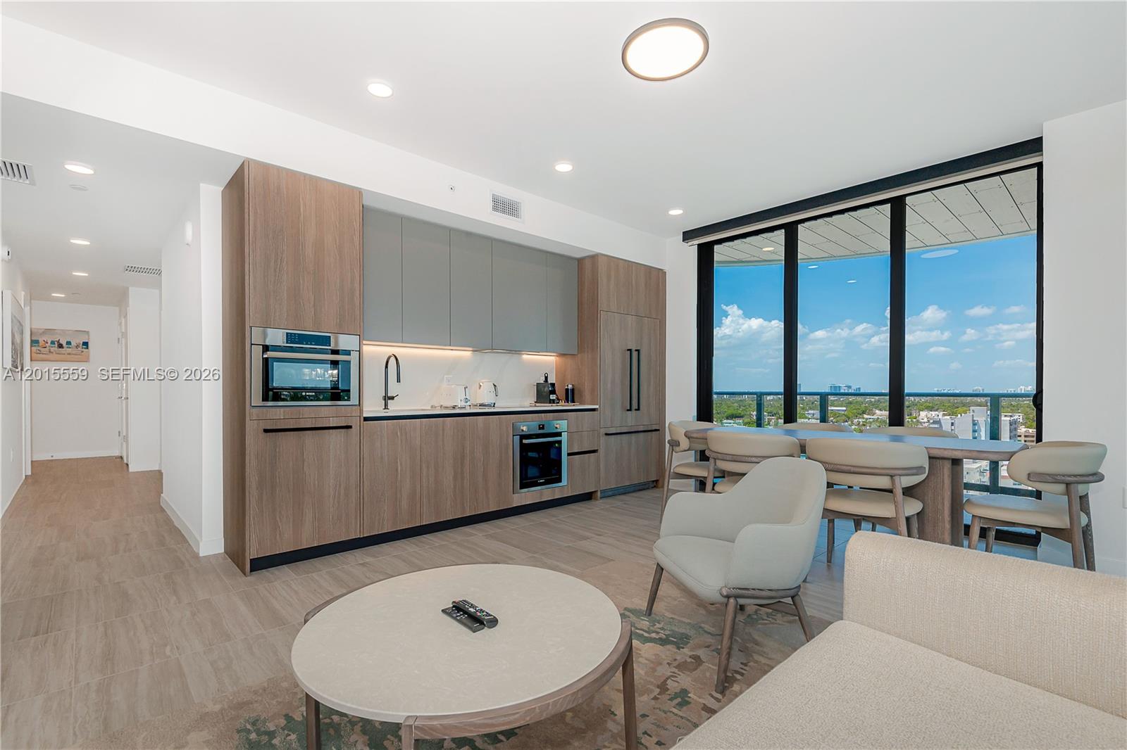 A modern kitchen and living area features wood cabinetry, stainless appliances, and floor-to-ceiling windows — 580 72nd St # 1112, Miami Beach FL 33141, MIAMI BEACH, FL