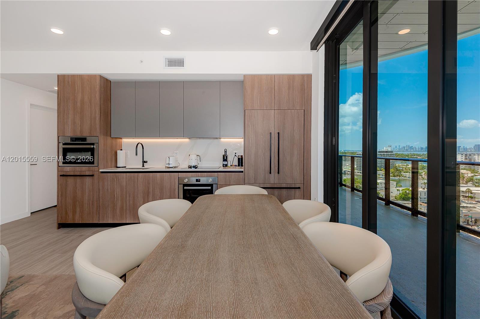 A modern kitchen features wood-grain cabinetry, gray upper cabinets, and a dining table with chairs — 580 72nd St # 1112, Miami Beach FL 33141, MIAMI BEACH, FL